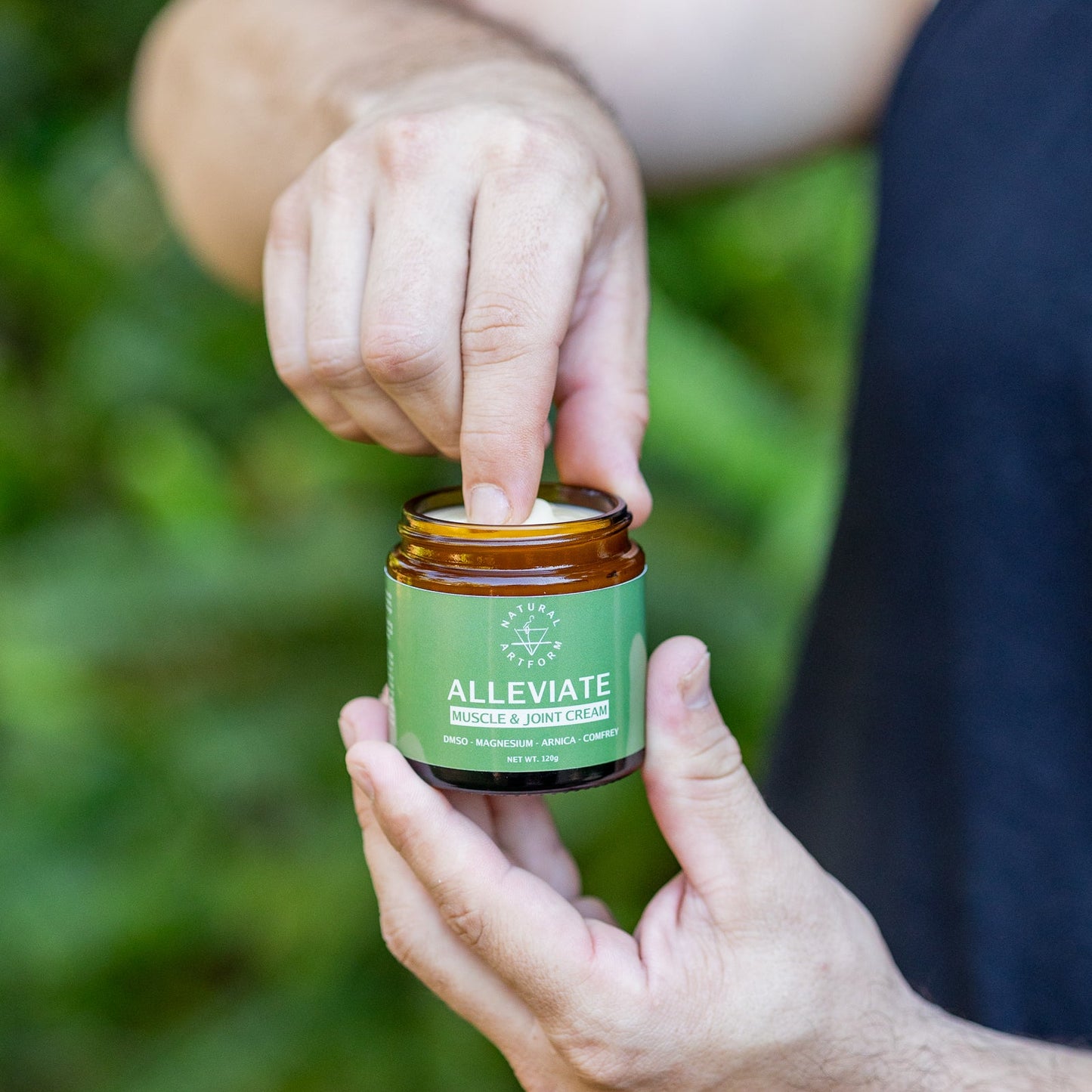 Person applying cream from a jar labeled 'Alleviate' against a blurred green background