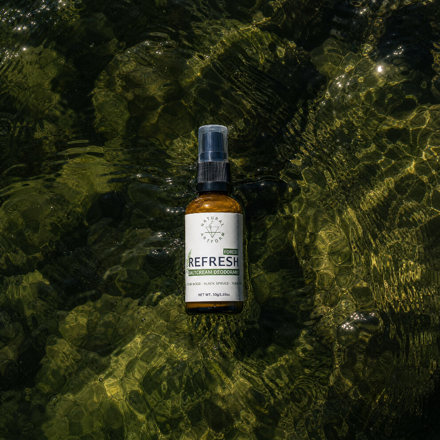 A small amber spray bottle labeled 'Pura REFRESH' and 'Forest Stream' floating on the surface of shallow, sunlit water with rippling reflections.
