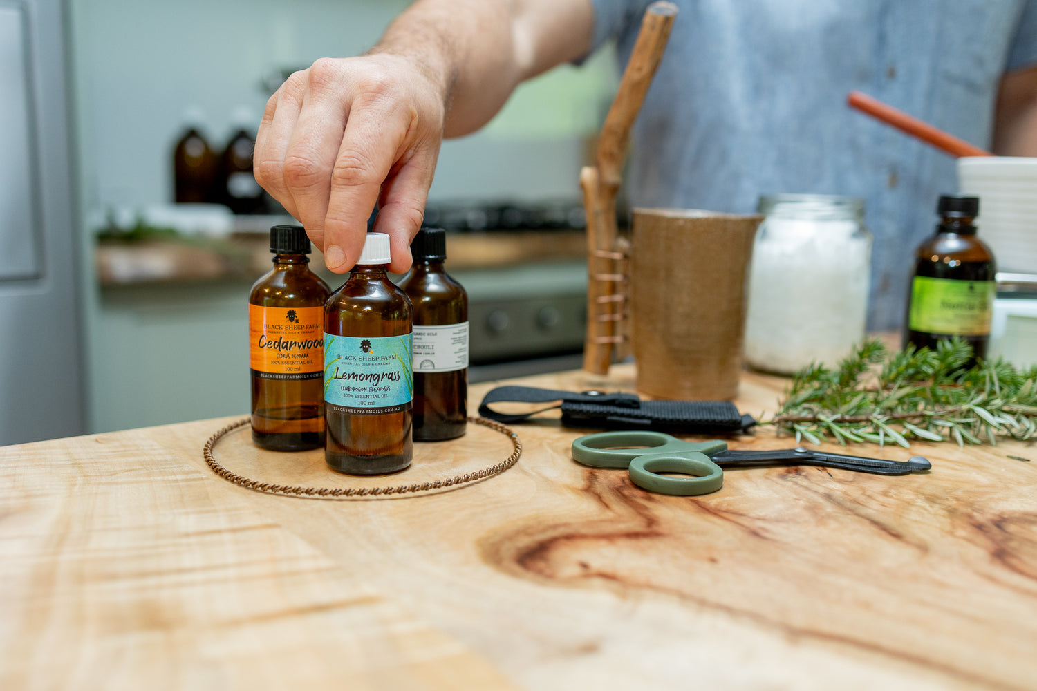 Hand selecting a bottle of essential oil from a wooden surface with other bottles and herbs.